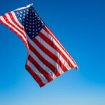 The American flag proudly waves on a flagpole against a clear blue sky, symbolizing freedom and patriotism.